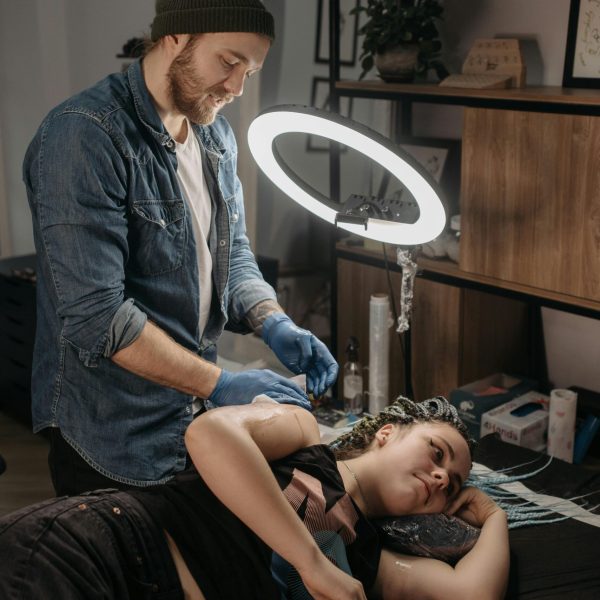 A tattoo artist creating a new design on a woman's arm in a modern studio setting.